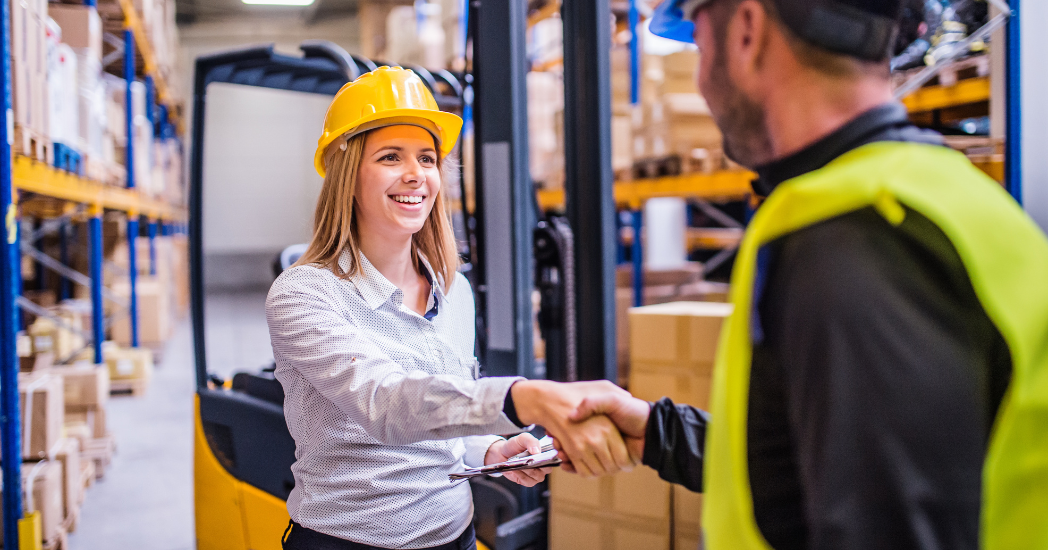 Women shaking hands with a man in a warehouse.