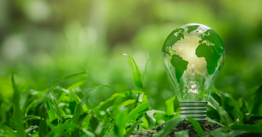 Green energy concept. Light bulb with the world inside of it set on a grassy background. 
