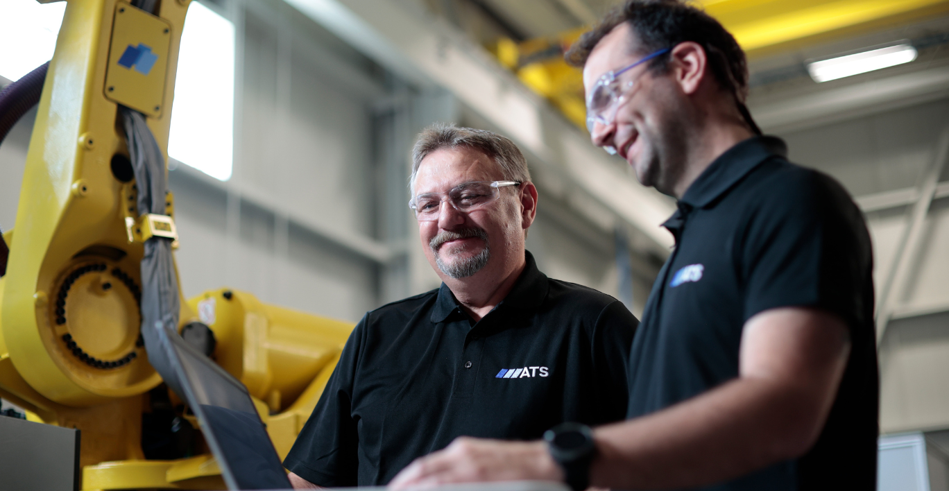 Two men reviewing data on a computer with a large yellow robot in the a background