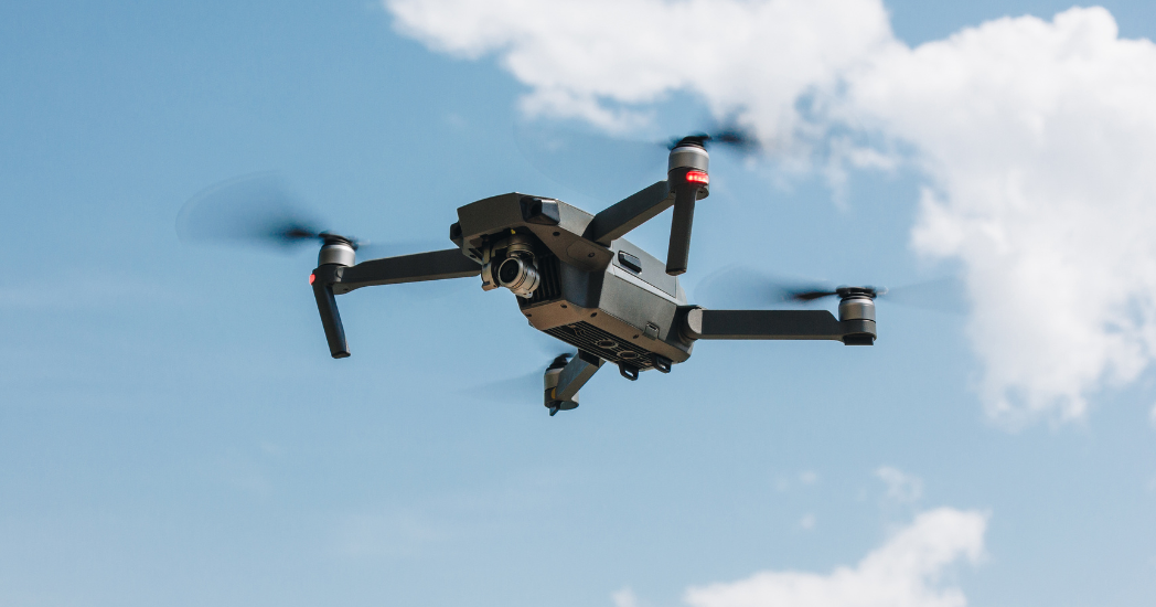 Drone flying with a blue sky in the background with white clouds on the right hand side of the image. 